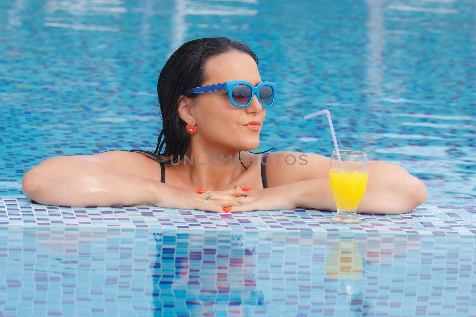 Woman drinking a fruit juice and enjoying in a swimming pool during a sunny day . Summer and holiday concept