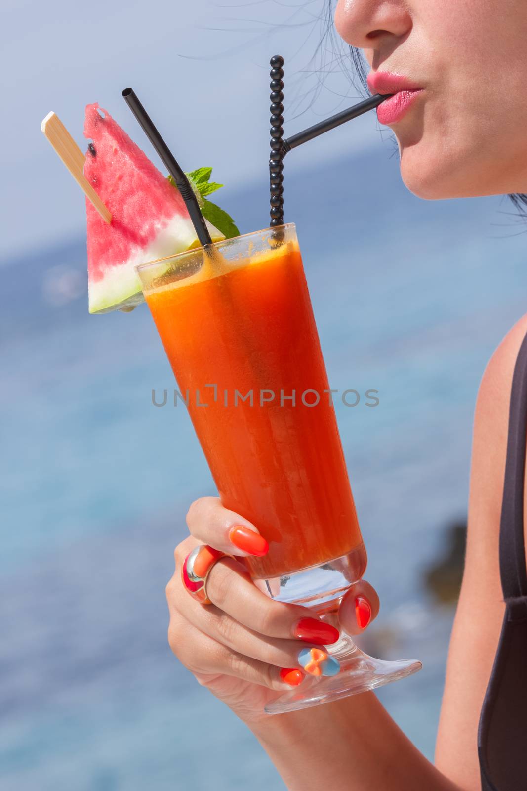 Woman with cocktail glass near sea. Blurred sea on background.