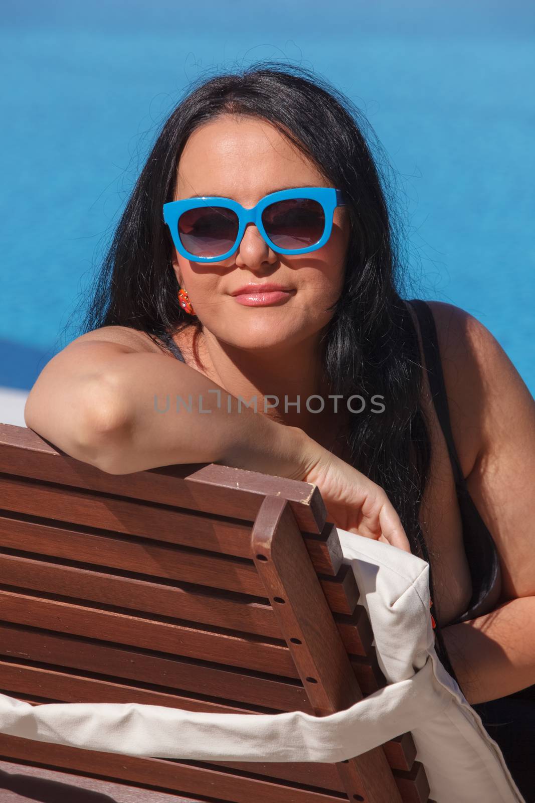 Woman in swimsuit with sunglasses laying on chaise-longue poolside and looking away. Done with a retro vintage  filter