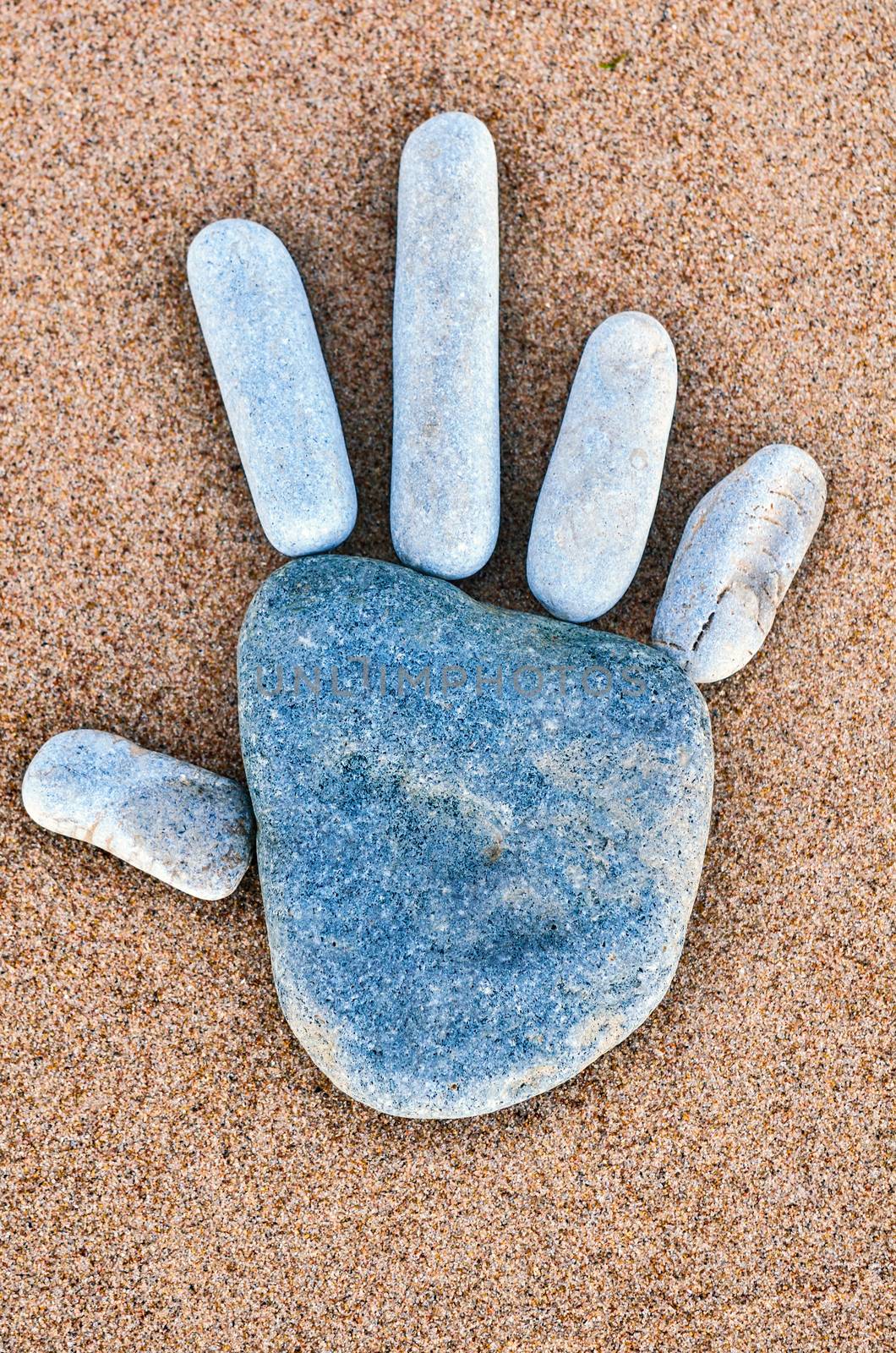 Hand print of pebbles on the sandy beach