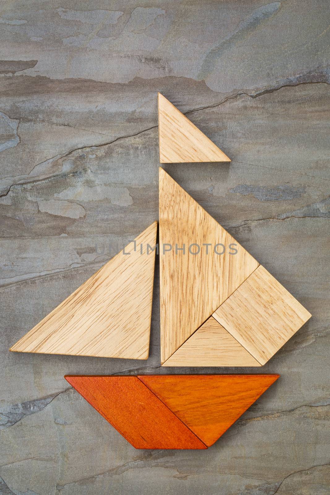 abstract picture of a sailing boat built from seven tangram wooden pieces over a slate rock background, artwork created by the photographer
