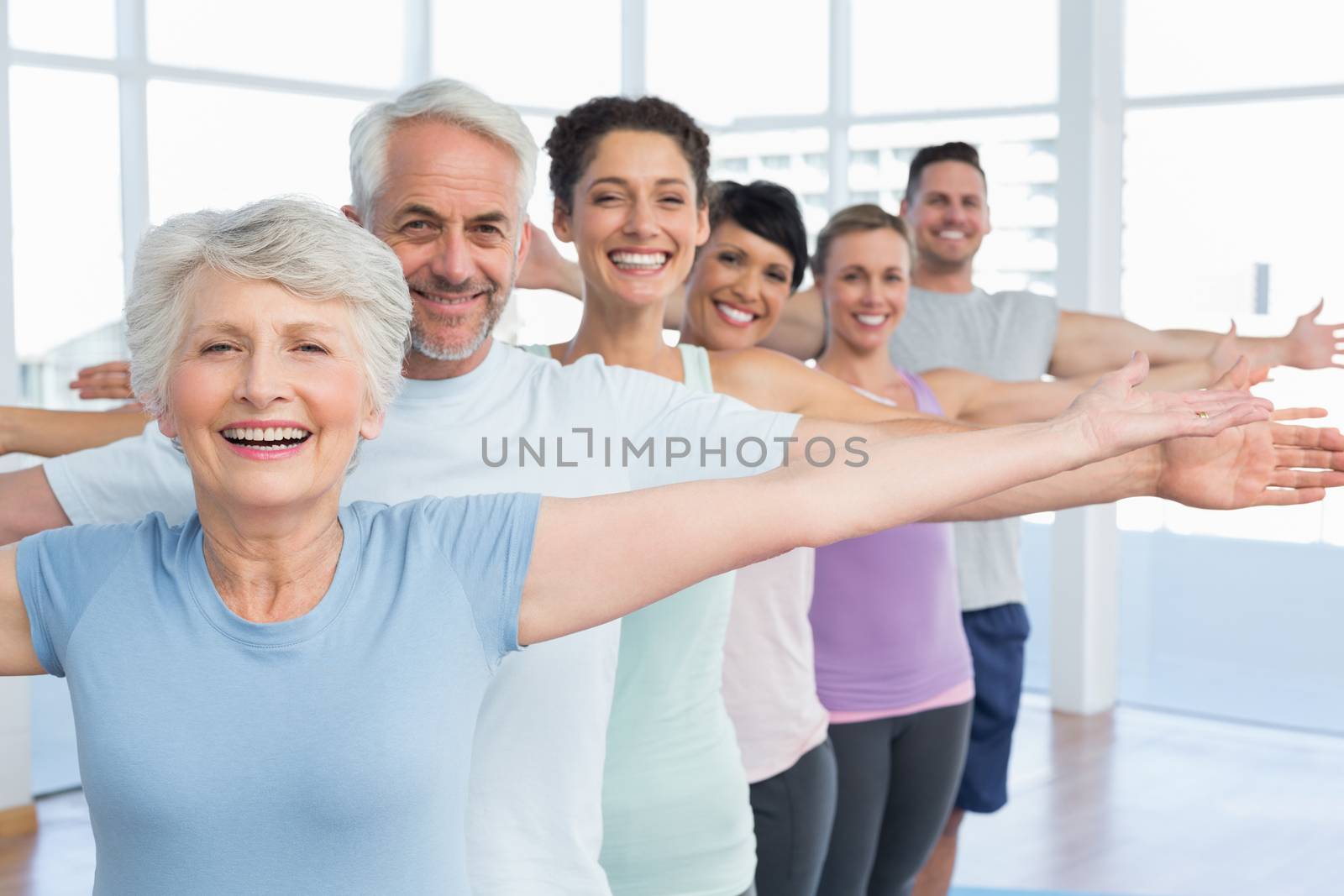 Portrait of fitness class stretching hands in row at yoga class