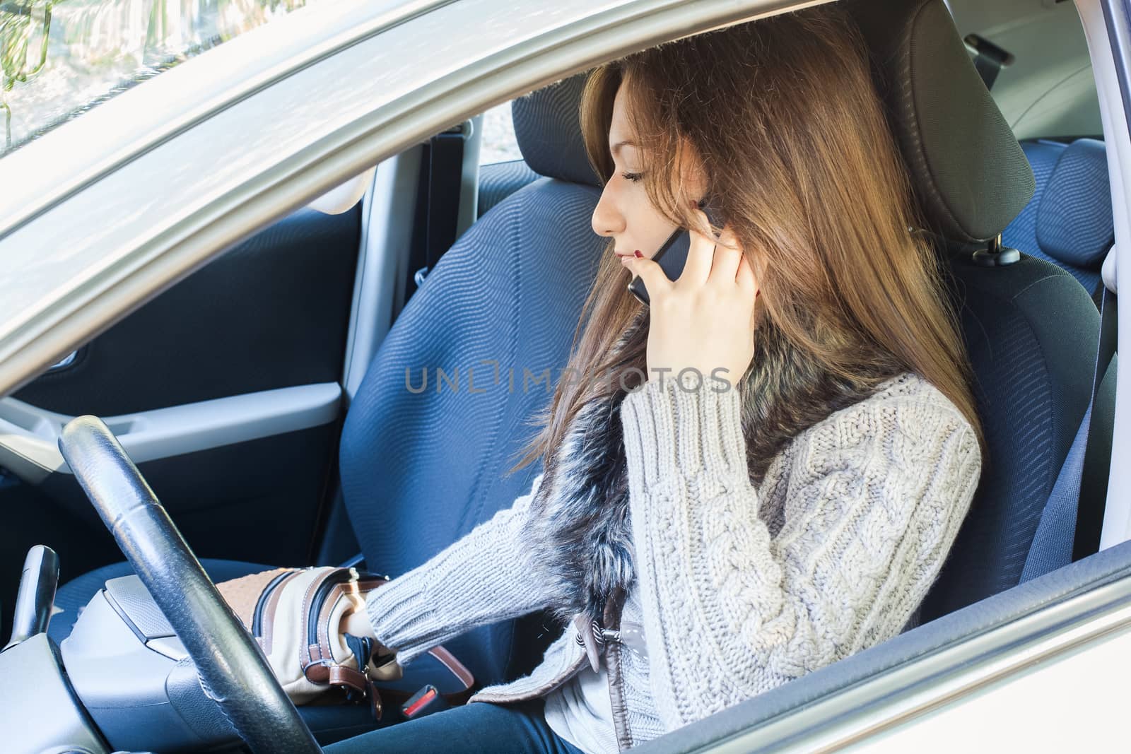 Woman sitting in drivers seat of her car , talking to mobile phone and searching purse