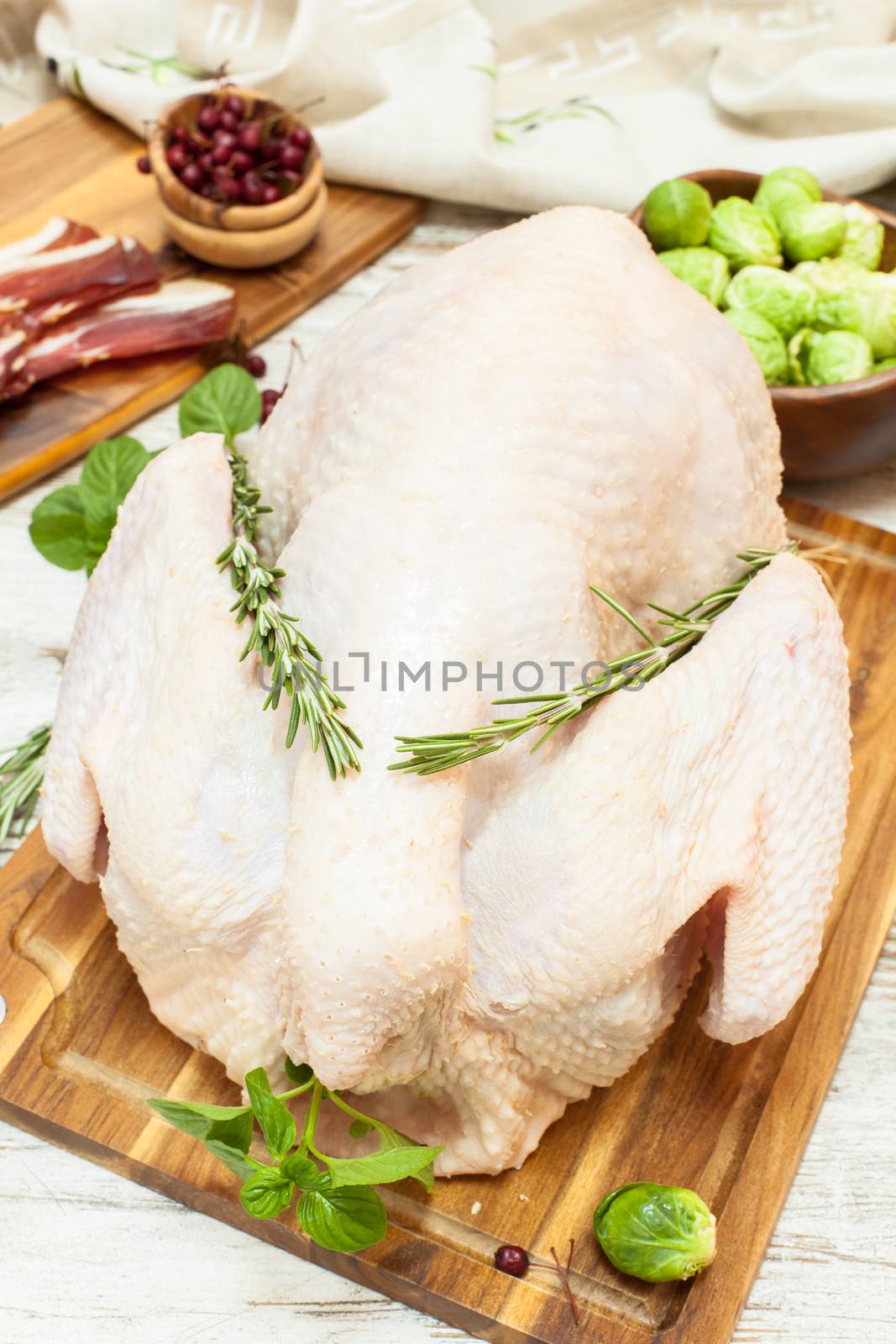 Whole raw turkey on wooden cutting board,vegetables, ham and spices. Viewed from above