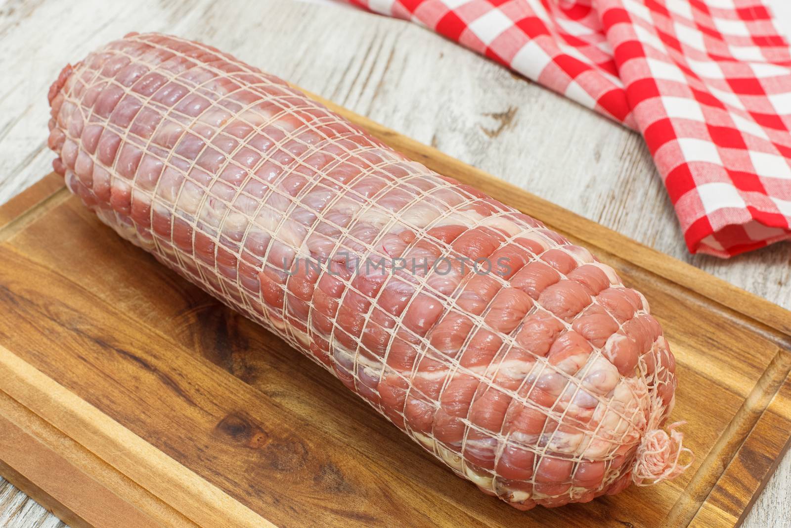 Raw rolled meat enclosed in tied netting. Raw rolled meat enclosed in tied netting. Roast of veal stuffed with bacon, ham and spices, ready to barbecue