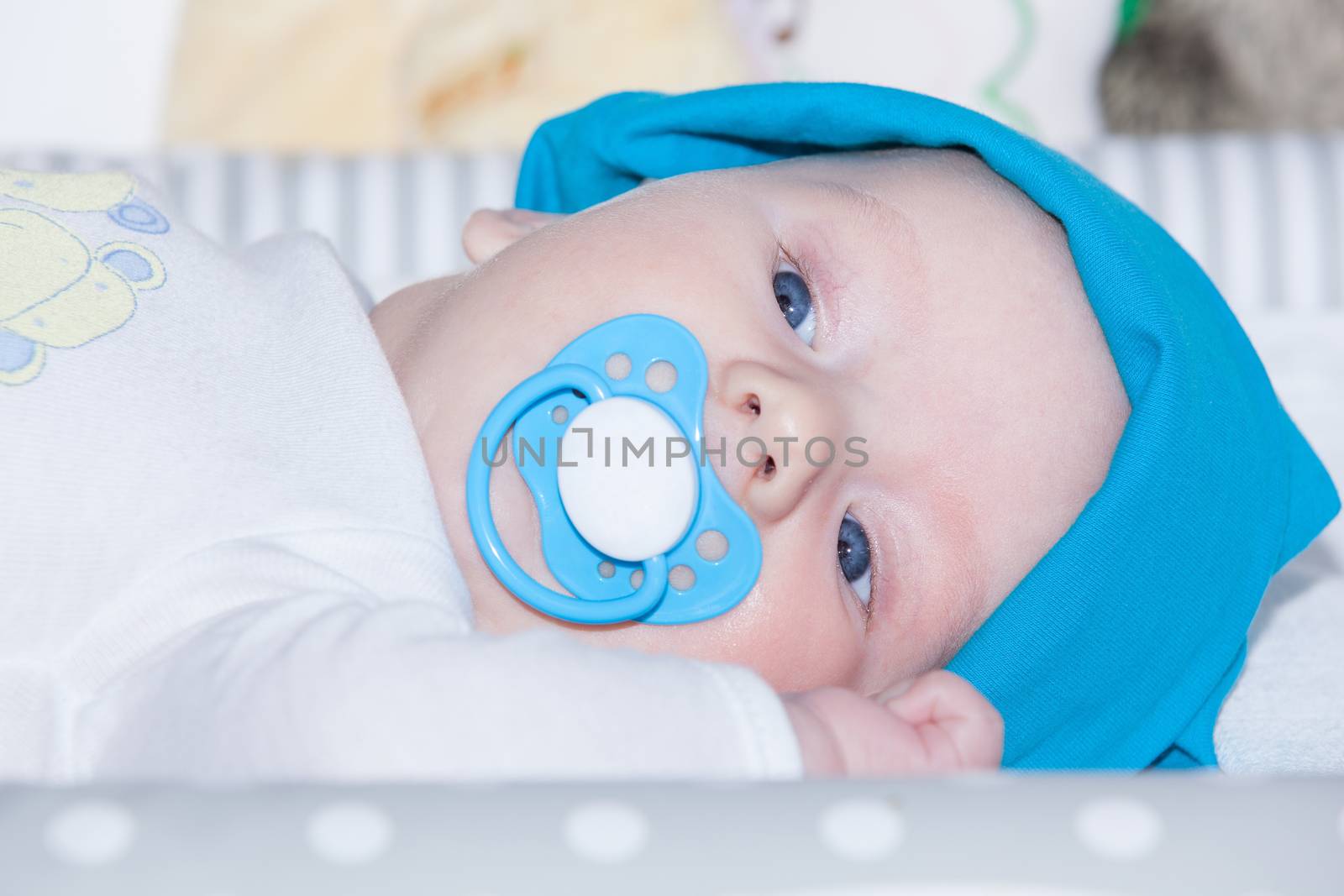 Caucasian 3 month old baby boy with big blue eyes and long eyelashes has a blue blanket and pacifer in his mouth