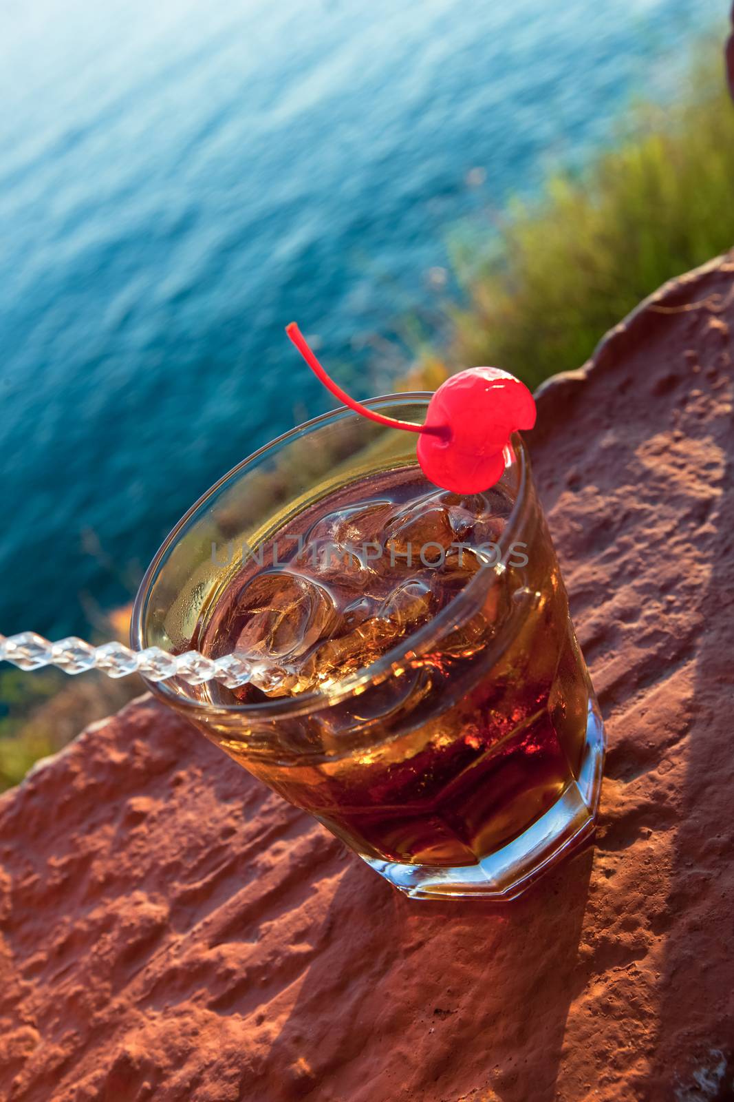 Manhattan cocktail garnished with a cherry. Cocktail against sea Outdoor composition during sunset lights