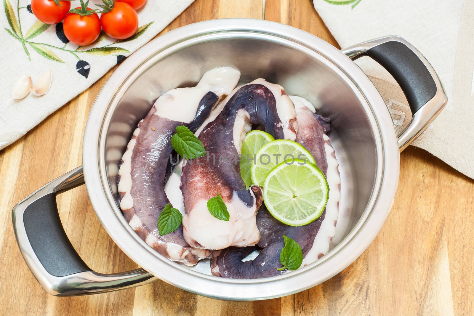 .Fresh octopus in a kitchen, with green basil and vegetable in stainless steel pot ready for barbecue or cooking.