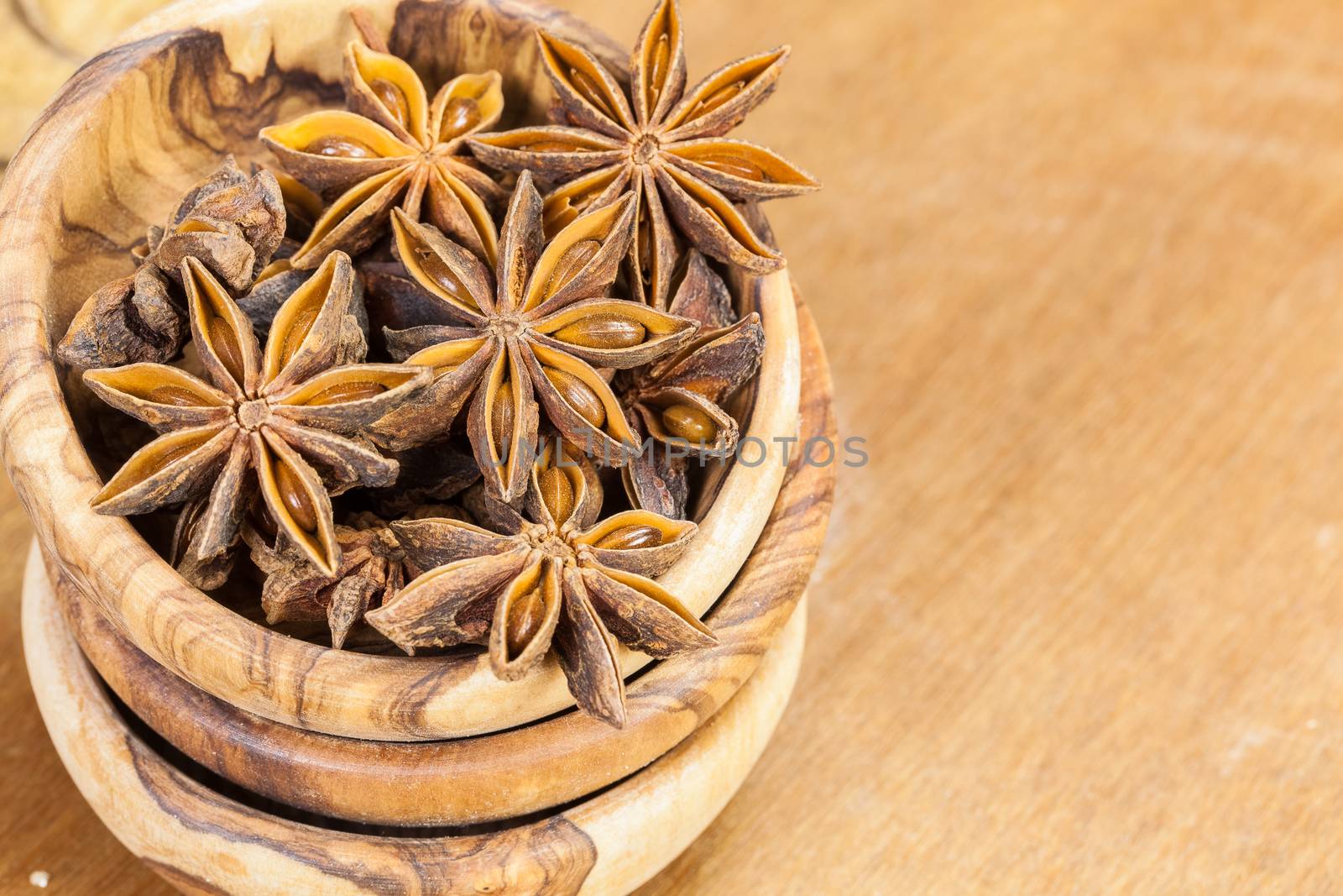 Star anise in olive wood bowl. Macro, viewed from above. Copy space composition