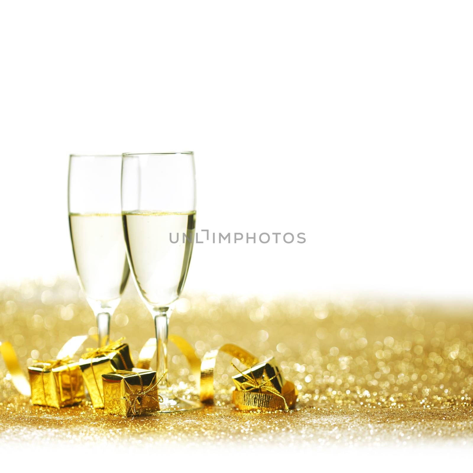 Glasses of champagne and decorative golden gifts isolated on white