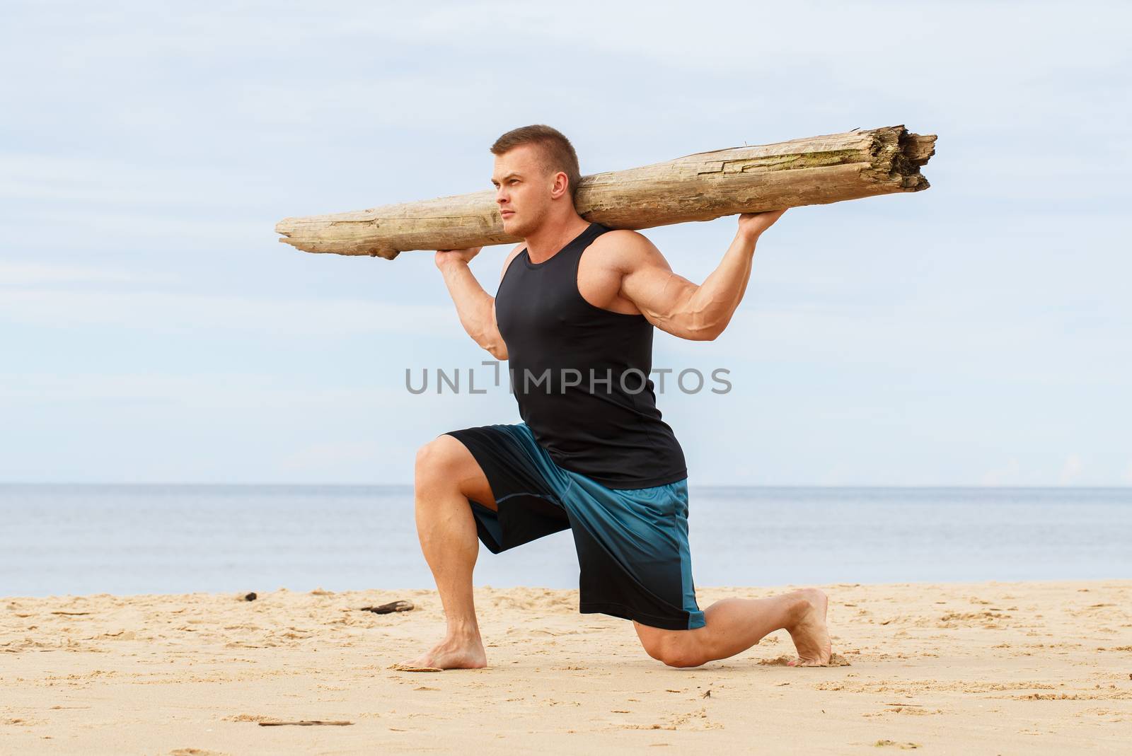 Sport, fitness. Bodybuilder with a big wood on the beach