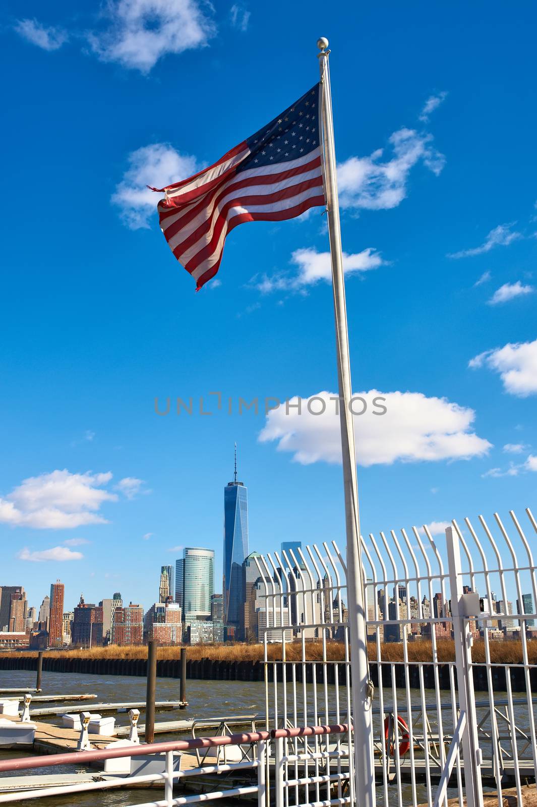 US American flag waving in the wind against blue sky with New York City Manhattan skyline at background 