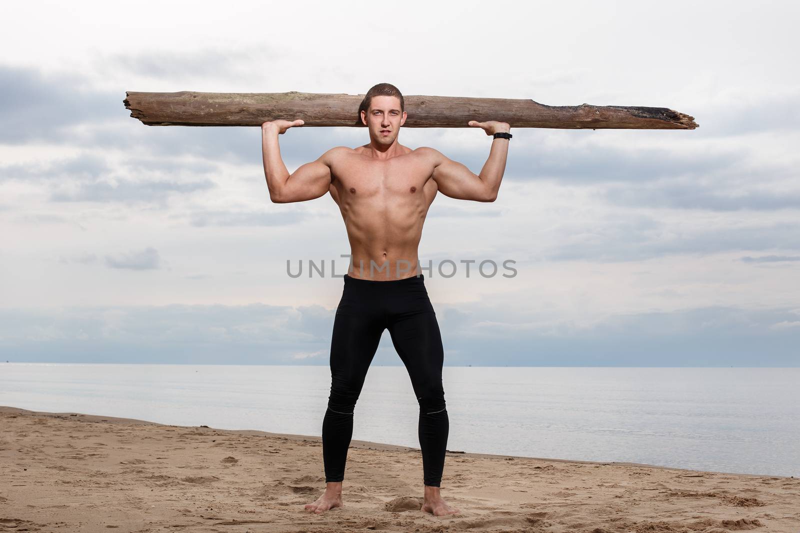 Sport, fitness. Bodybuilder with a big wood on the beach