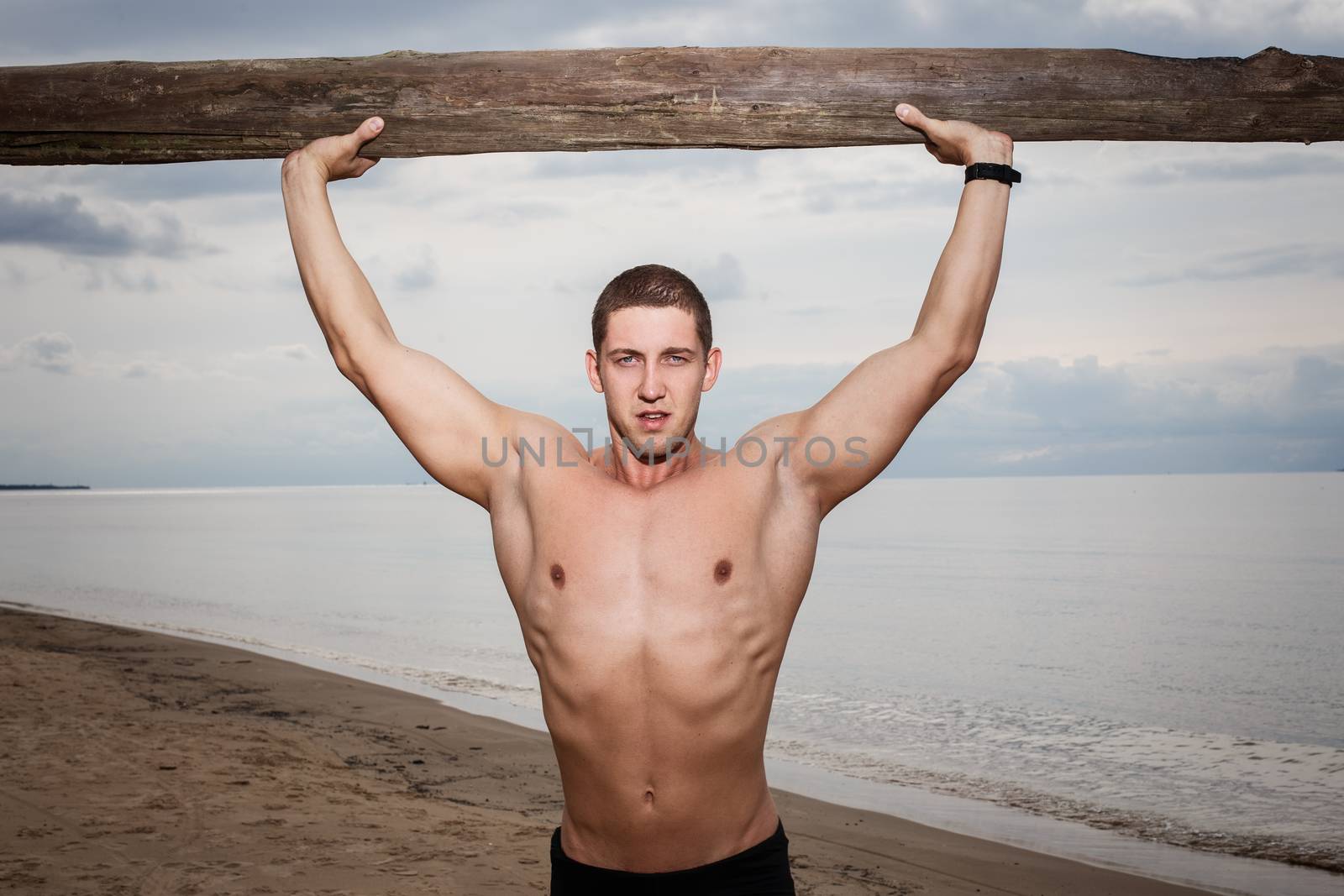 Sport, fitness. Bodybuilder with a big wood on the beach