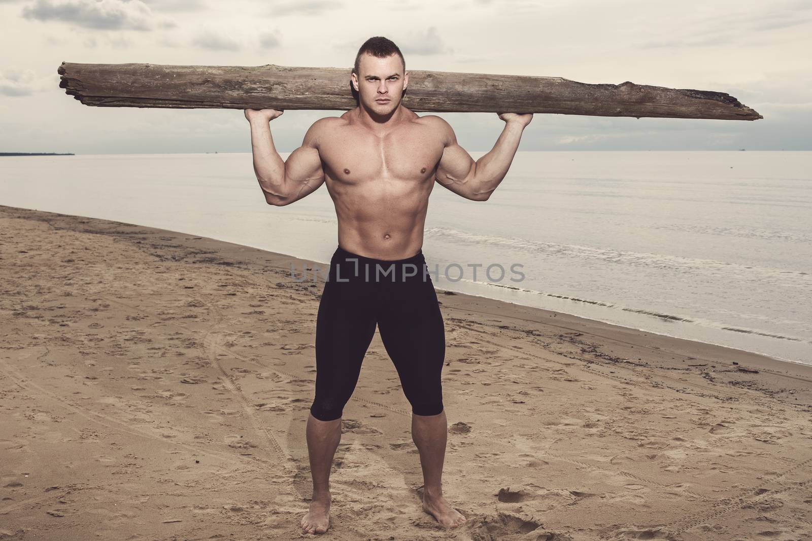 Sport, fitness. Bodybuilder with a big wood on the beach