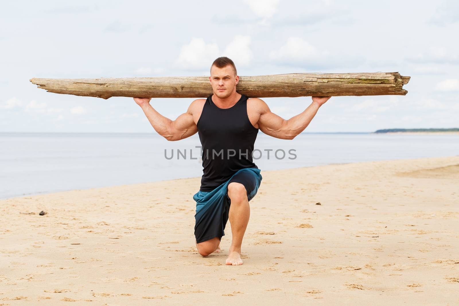 Sport, fitness. Bodybuilder with a big wood on the beach