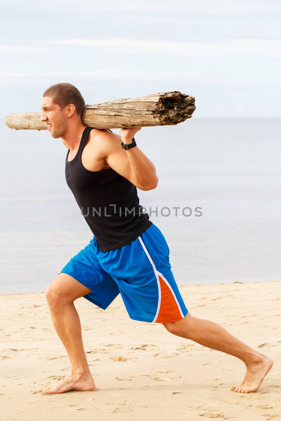 Sport, fitness. Bodybuilder with a big wood on the beach