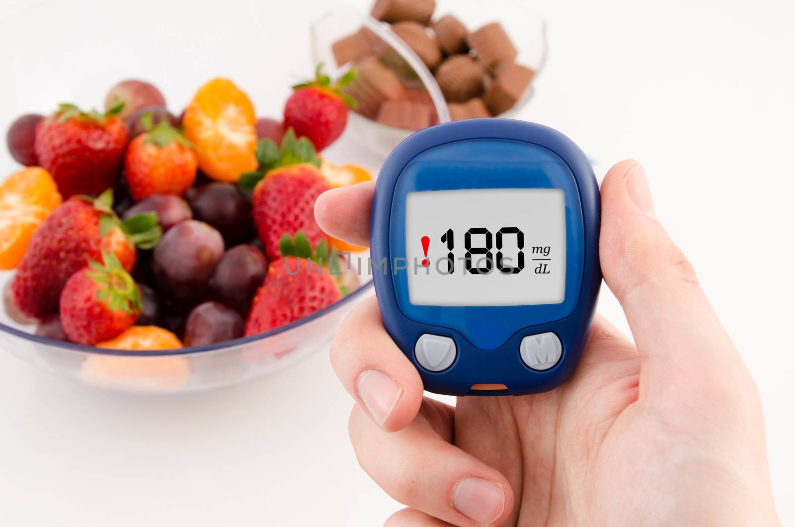 Hand holding meter with warning glucose level test. Fruits in background