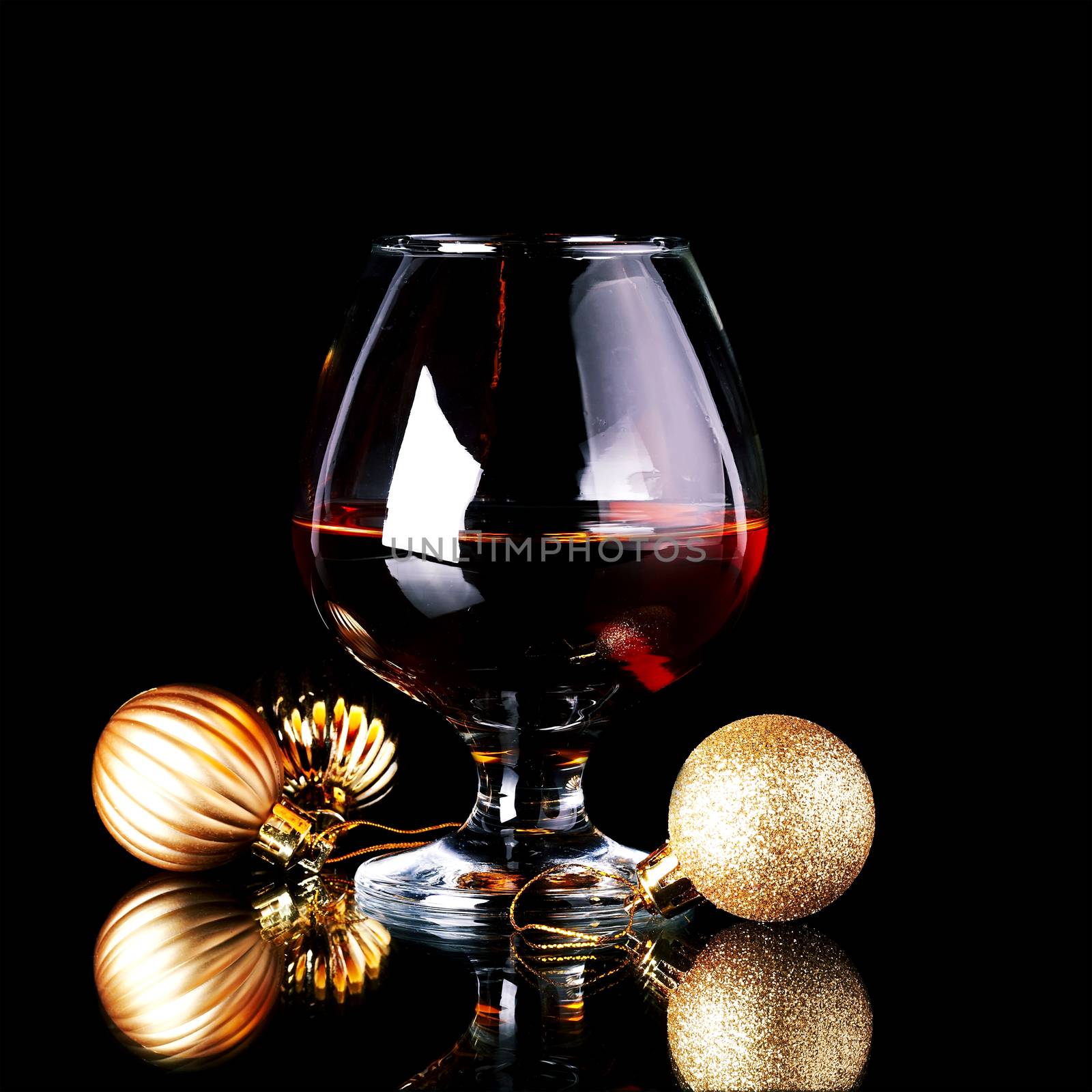 Glass with drink and a Christmas balls on a black background. New Year's balls and glass. Glass with alcohol and a Christmas ball.