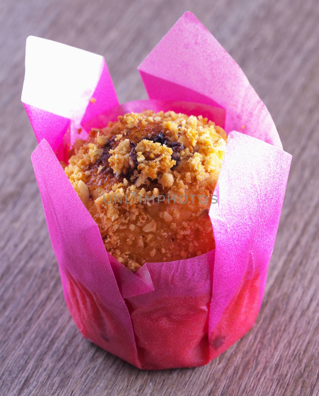 Chocolate muffin inside white and pink paper, over wooden table