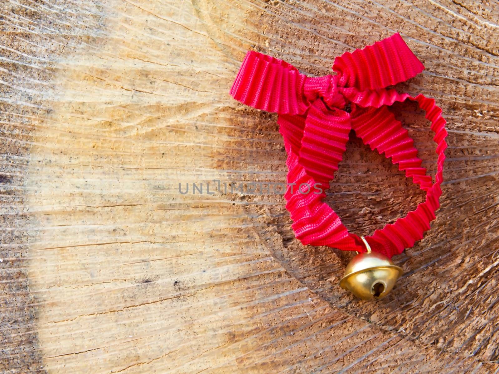Photo shows detail of jingle bell with red ribbon in the wood