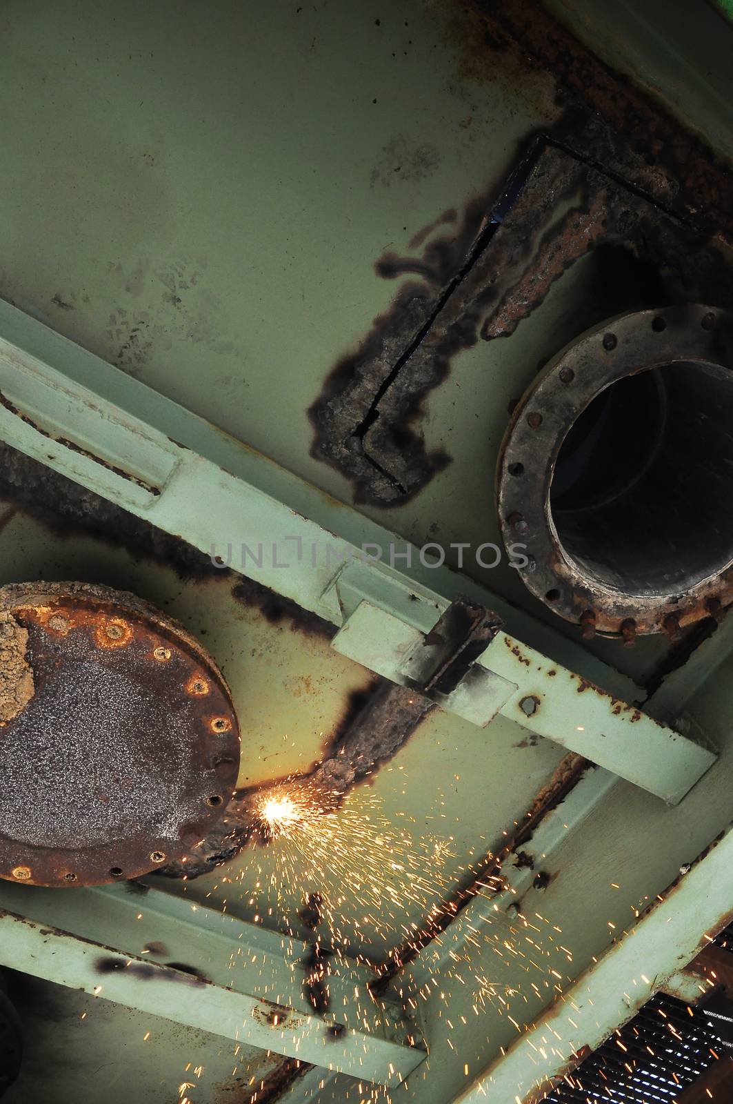 A small glowing flame underneath a steel structure in the process of being cut up and demolished by an acetylene torch, out of sight.
