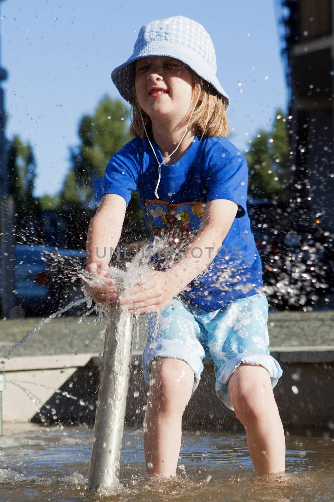 Boy in Cap Squirting Water from Fountain in Outdoor Pool