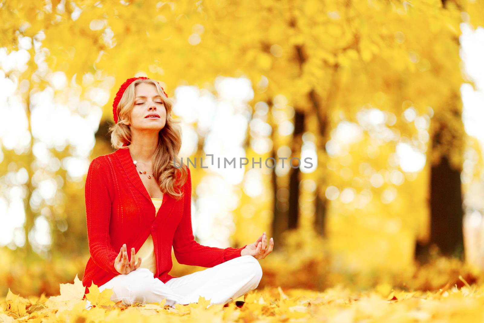 Beautiful young woman sitting in autumn park in lotus yoga position