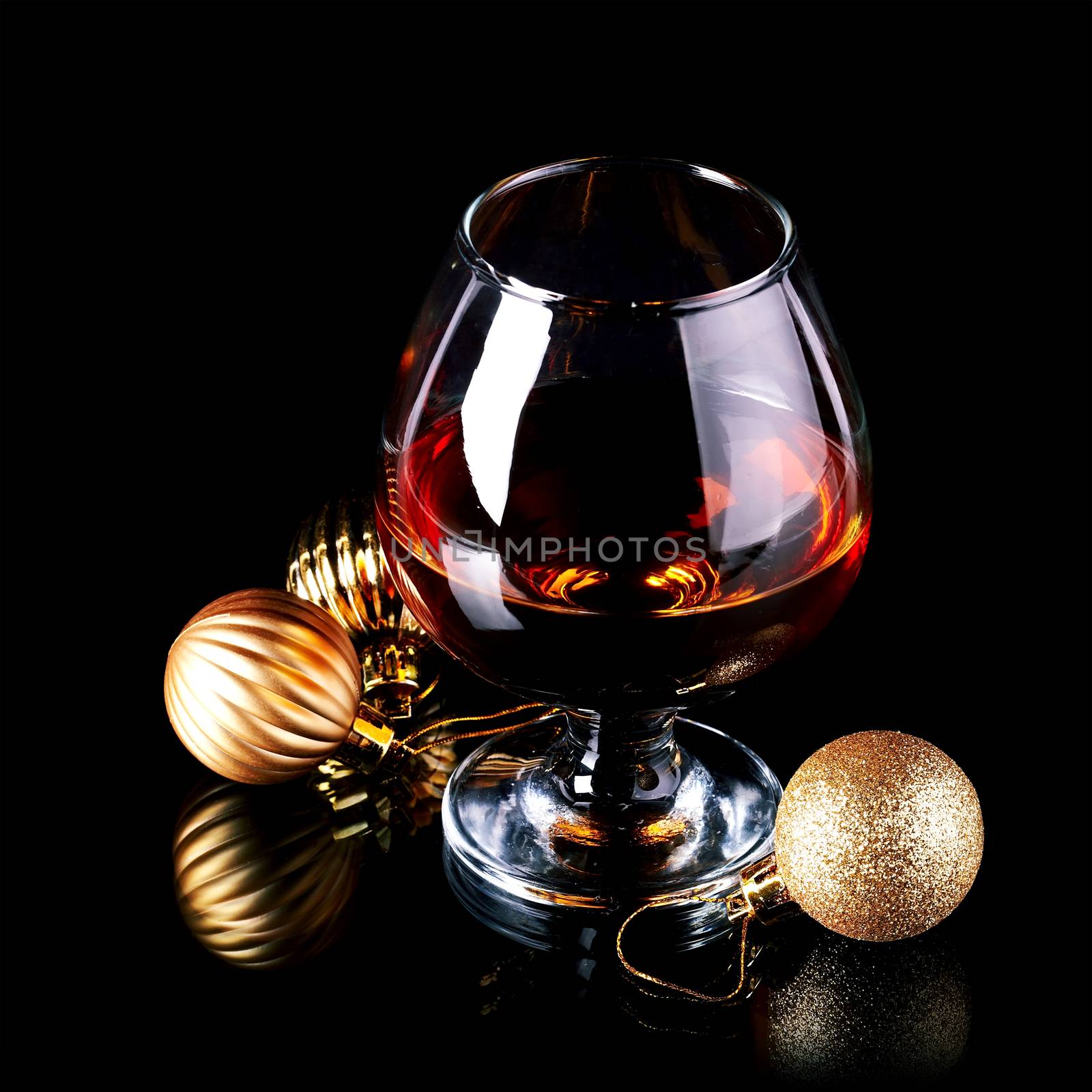 Glass with drink and a Christmas balls on a black background. New Year's balls and glass. Glass with alcohol and a Christmas ball.