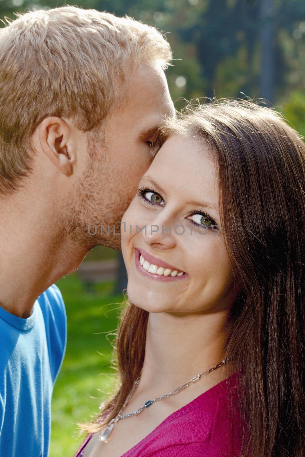 Young Girl Smiling as her Boyfriend Whispers in her Ear.