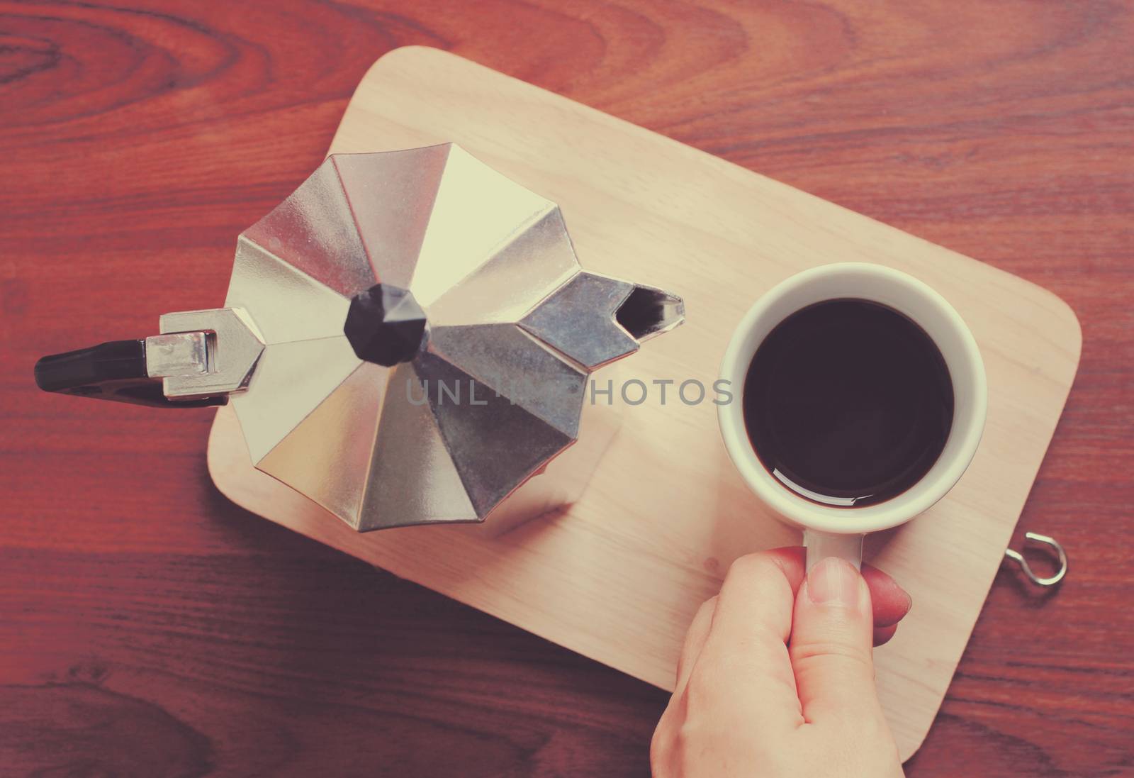 Hand holding coffee cup and moka pot with retro filter effect