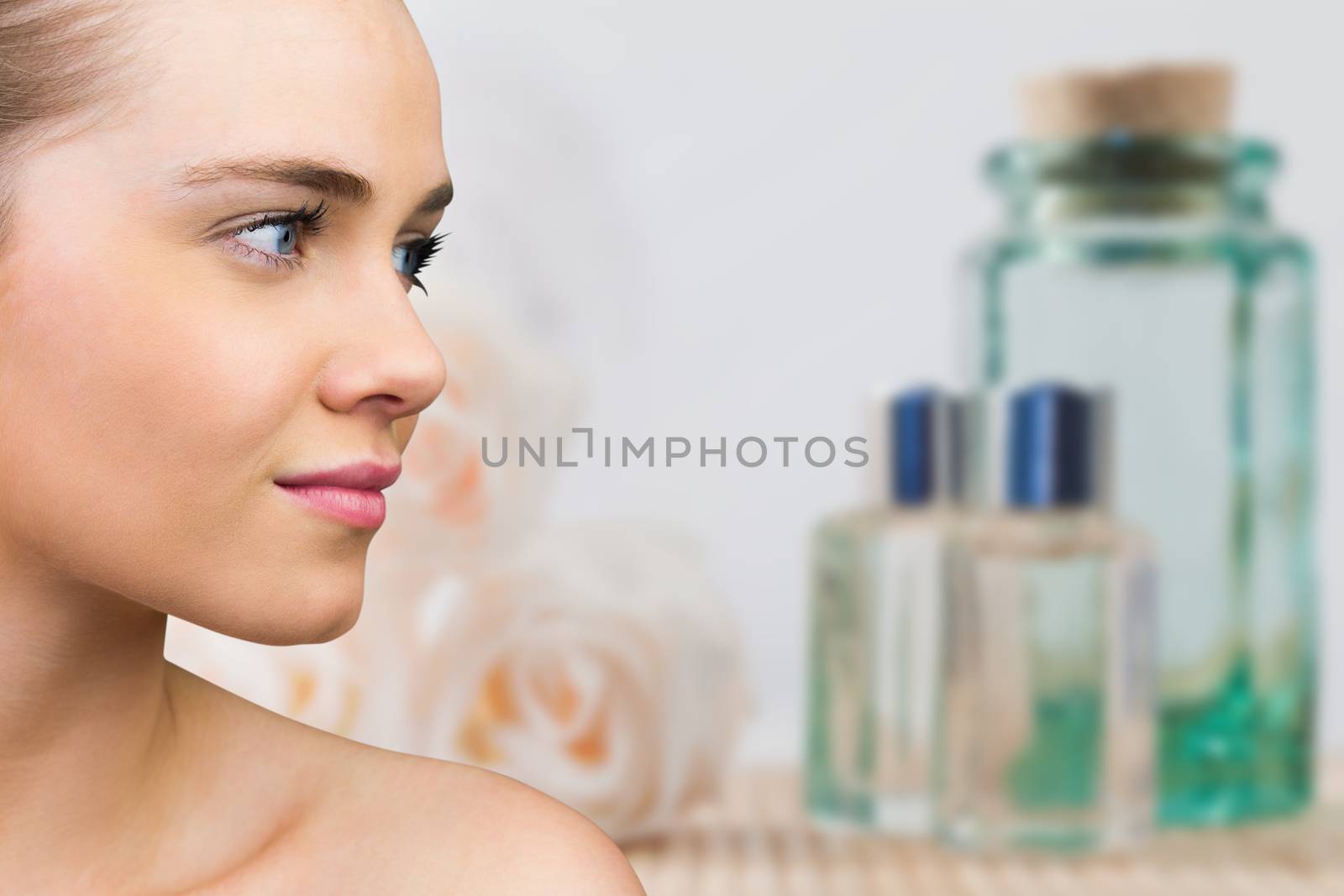 Smiling blonde natural beauty against glass jars and rose flowers in spa