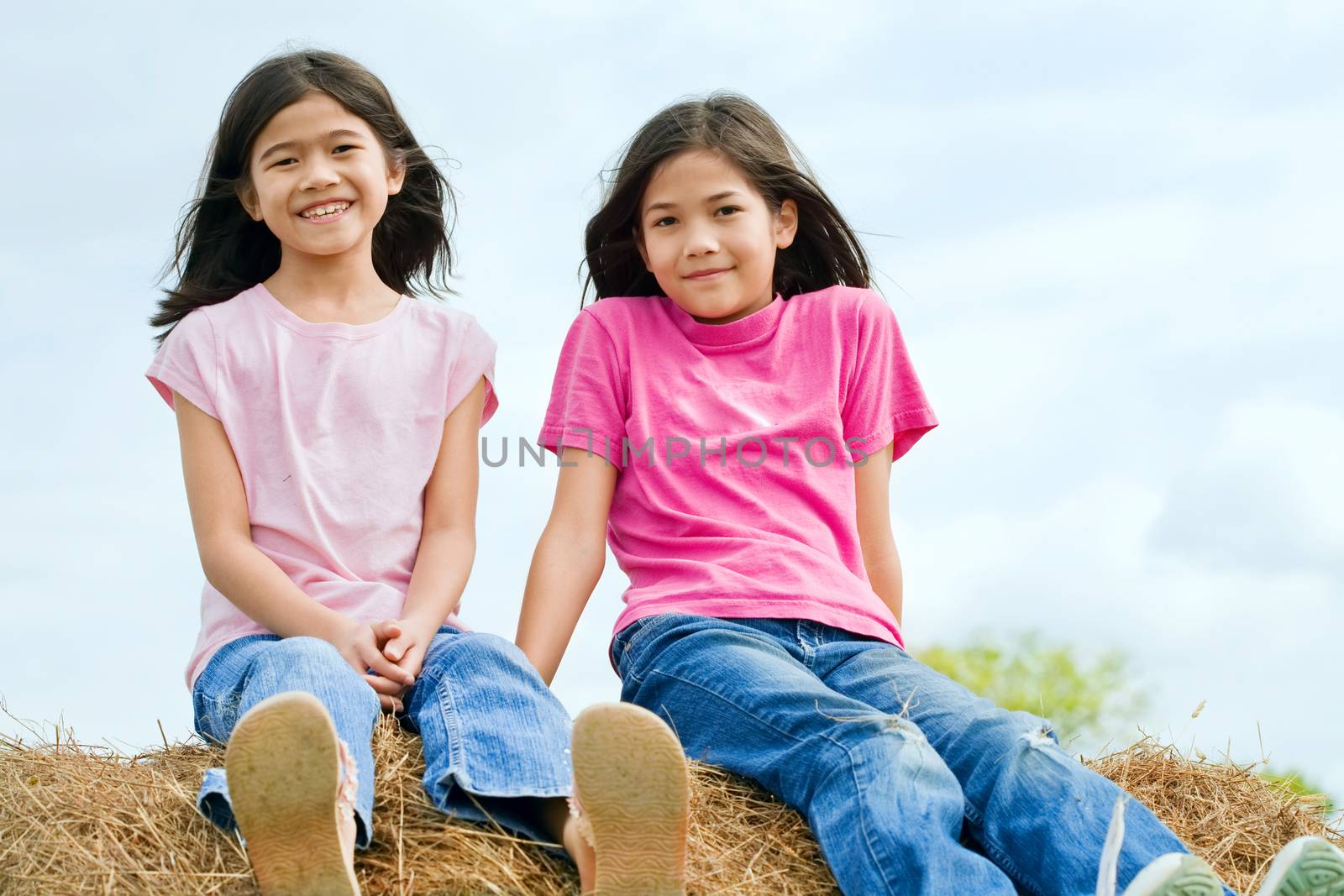 two young girls sitting on top of haybale by jarenwicklund