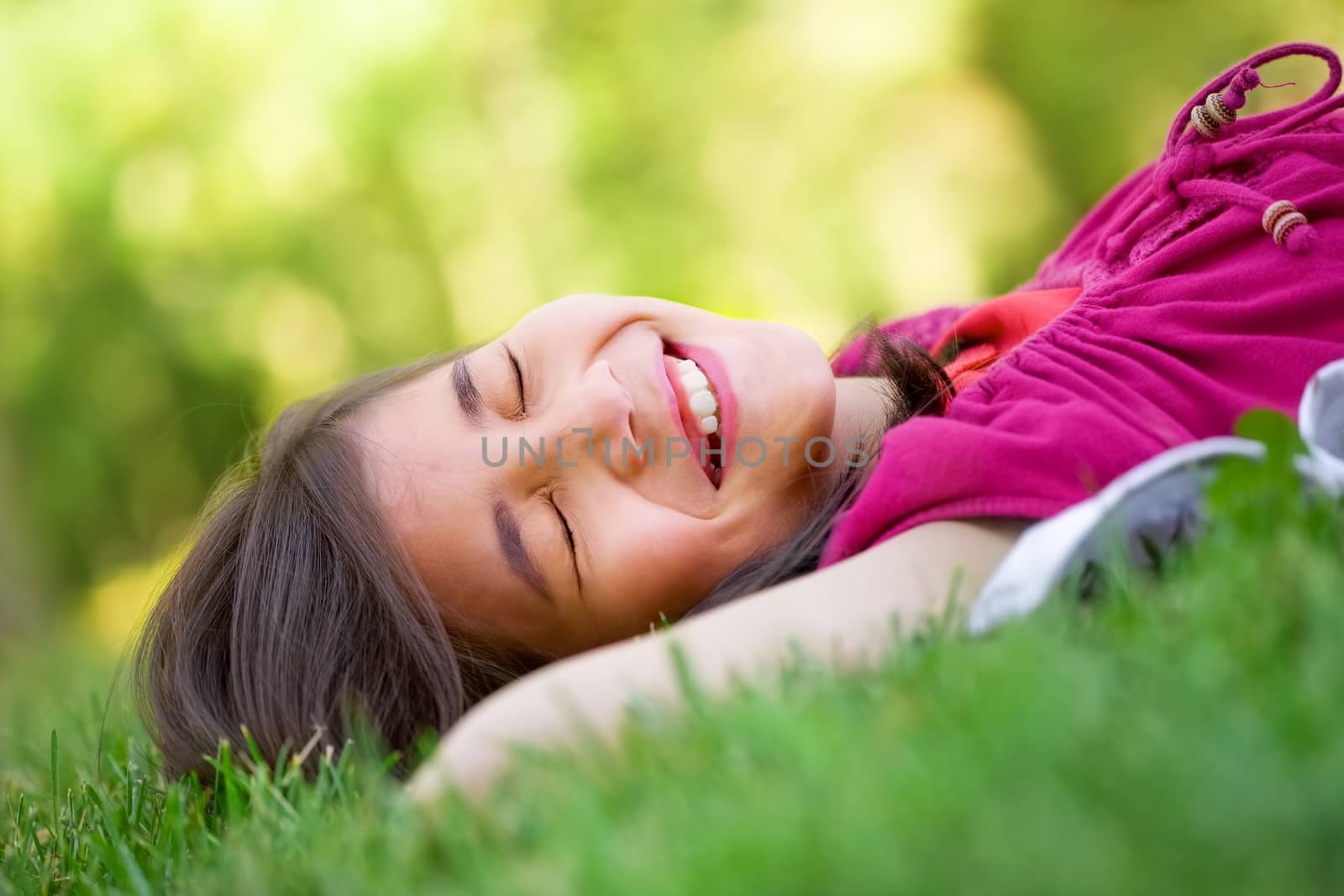 Little girl lying on grass lawn smiling with eyes closed, laughing