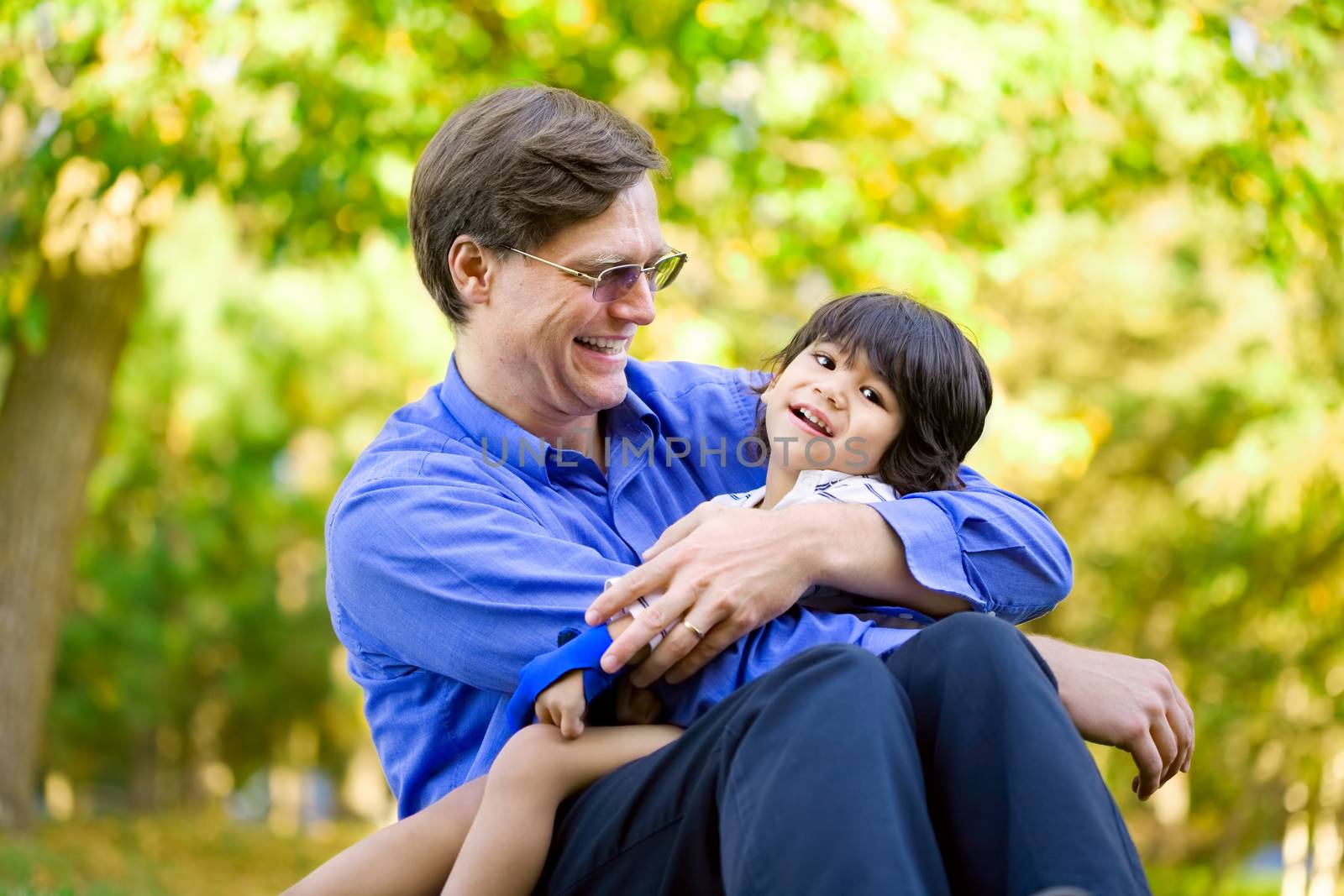 Businessman holding his disabled son on grass. Child has cerebral palsy.