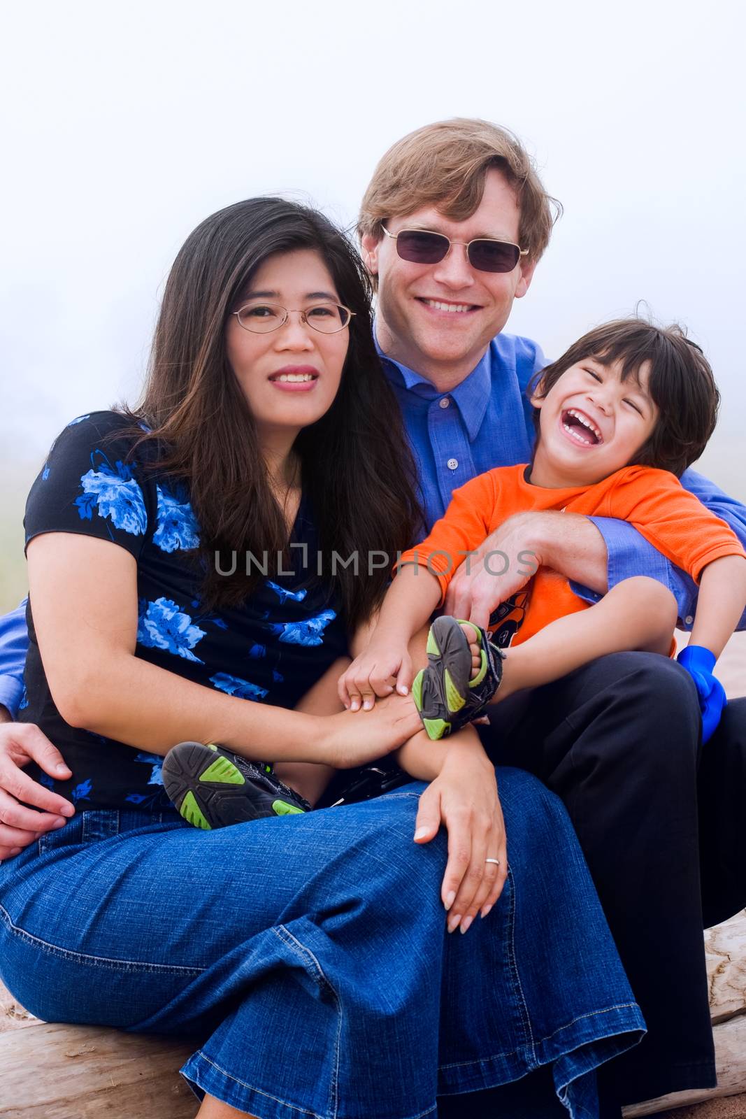 Mutiracial family sitting on beach on misty, foggy day.