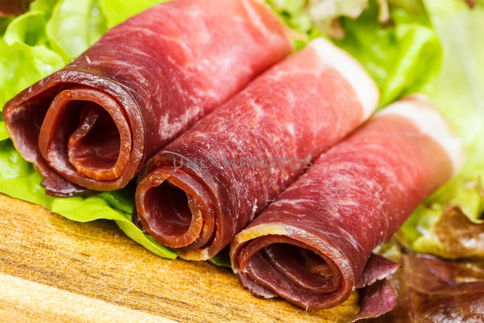 Slices of prosciutto rolled up and arranged on a lettuce leaf.