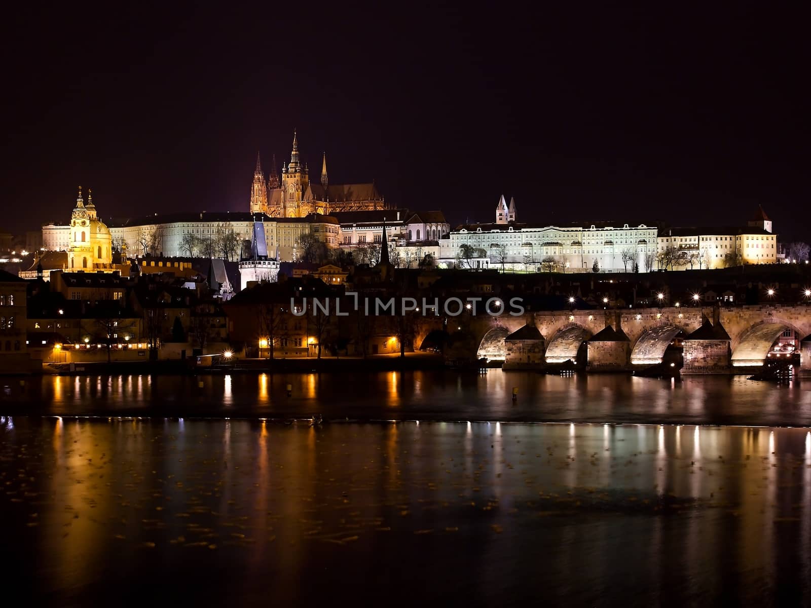 Photo shows night view of Prague Castle and bridge.