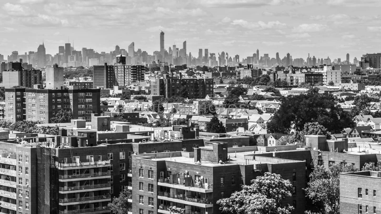 Aerial view of the buildings and streets of Rego Park area in Queens, with the skyscrapers of the city of Manhattan in the far background