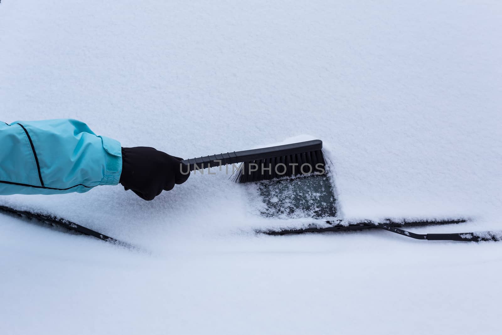 Woman cleaning snow from the car in the winter