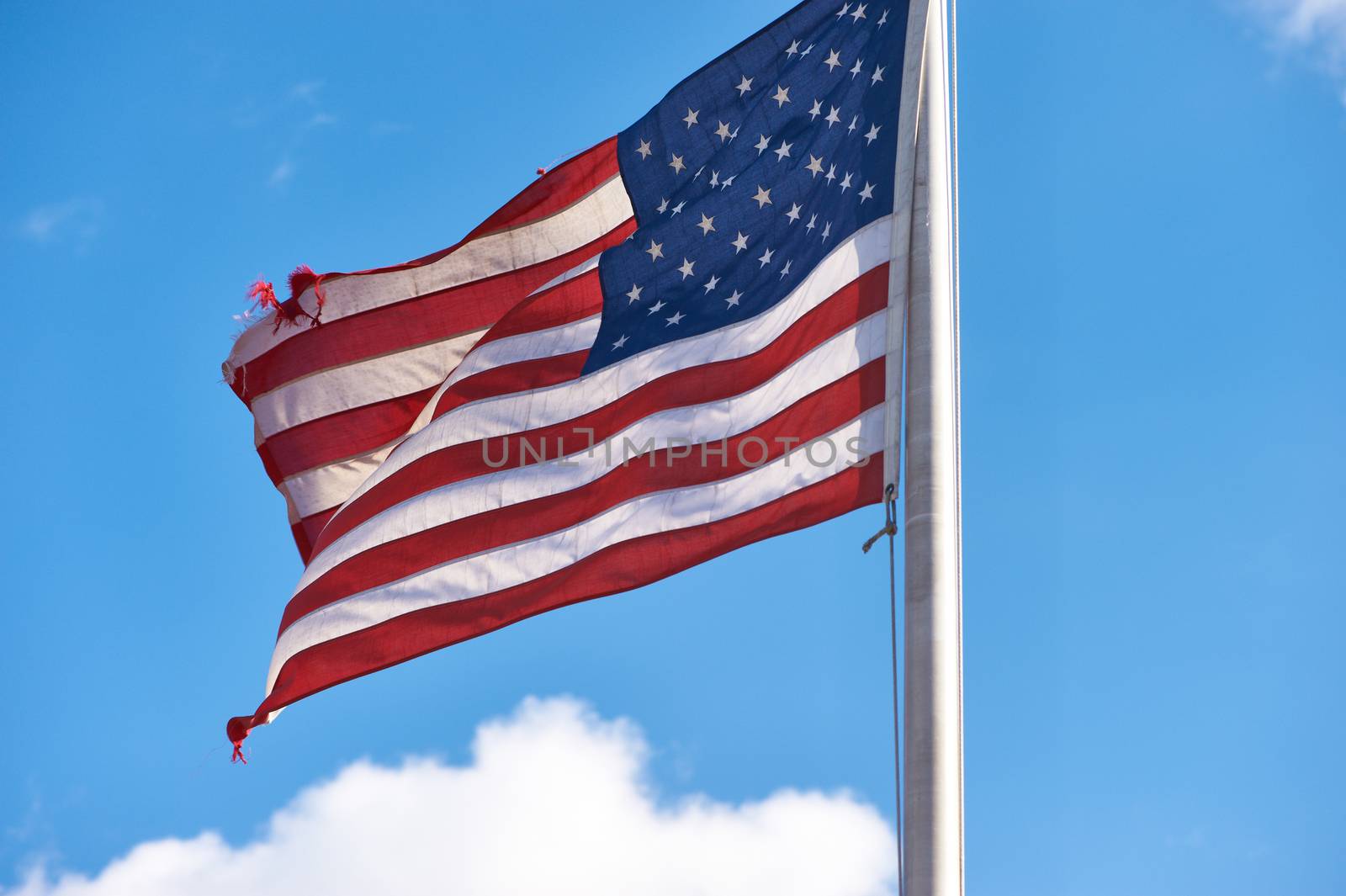 US American flag waving in the wind against blue sky and clouds