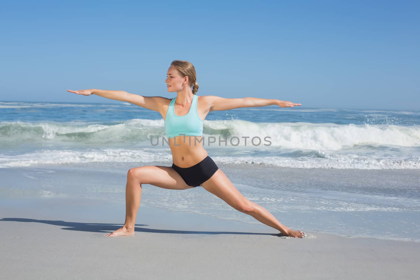 Fit woman standing on the beach in warrior pose on a sunny day