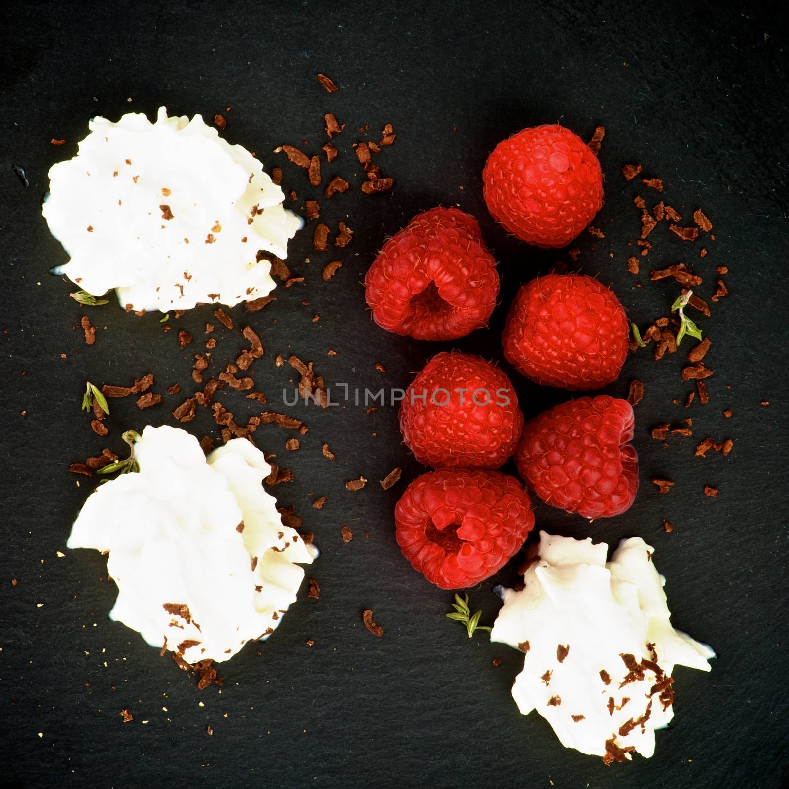 Delicious Dessert with Fresh Raspberries, Dairy Cream and Grated Dark Chocolate closeup on Black Plate. Top View