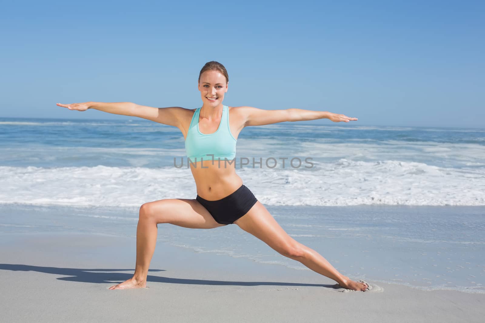 Fit woman standing on the beach in warrior pose on a sunny day