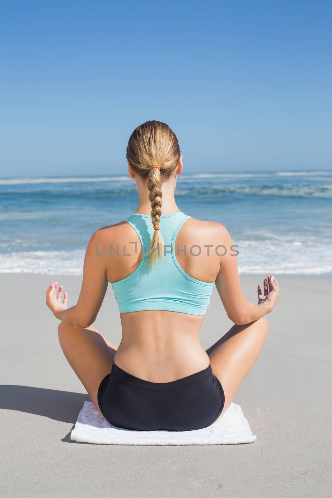 Fit woman sitting on the beach in lotus pose on a sunny day