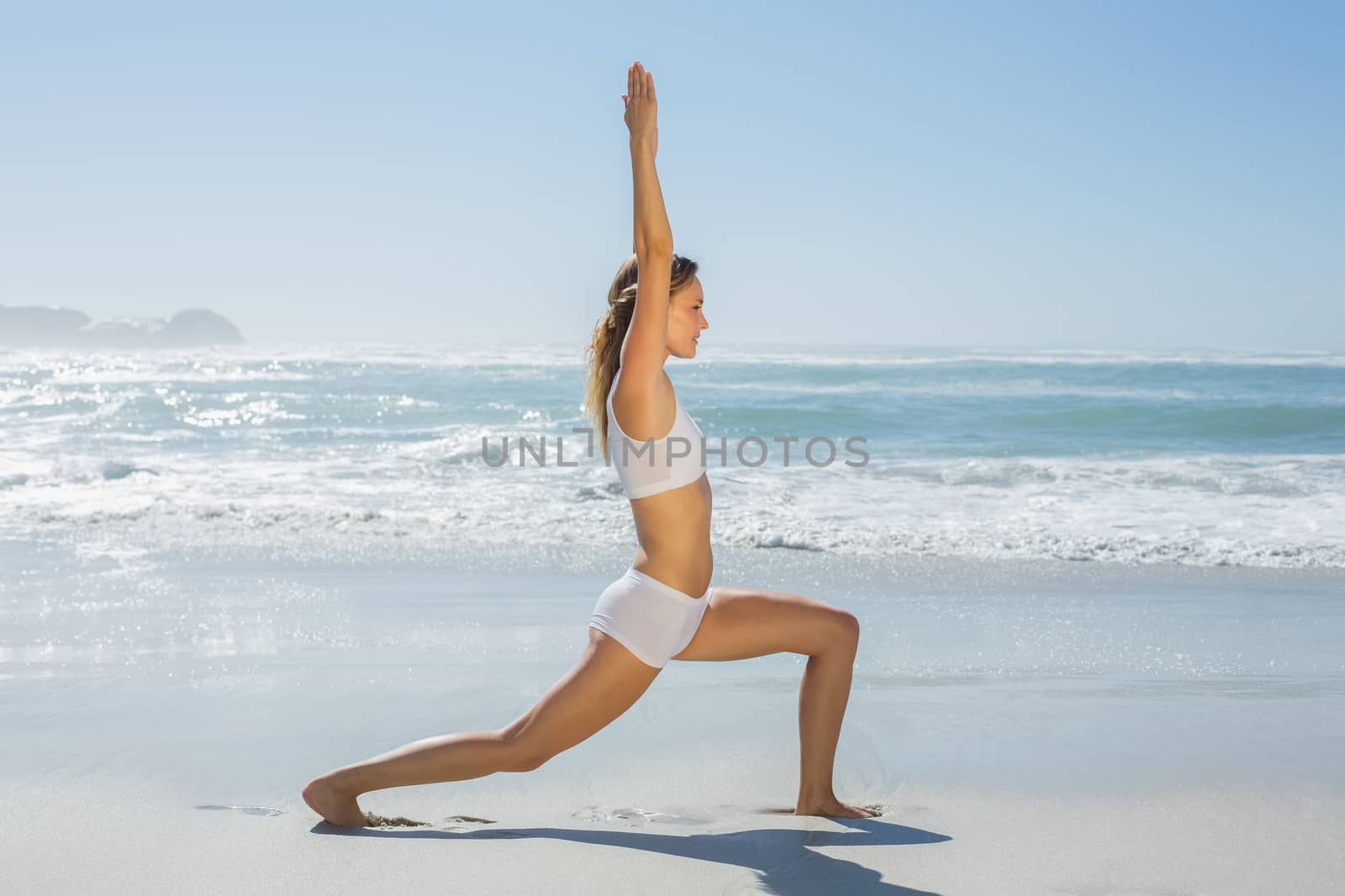 Gorgeous blonde in warrior pose by the sea on a sunny day