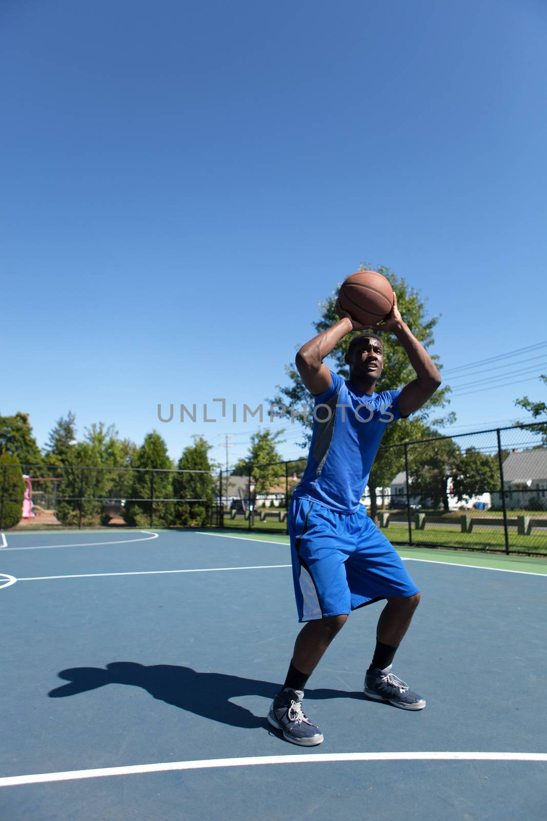 Young basketball player in his early twenties shooting the ball on an outdoor court.