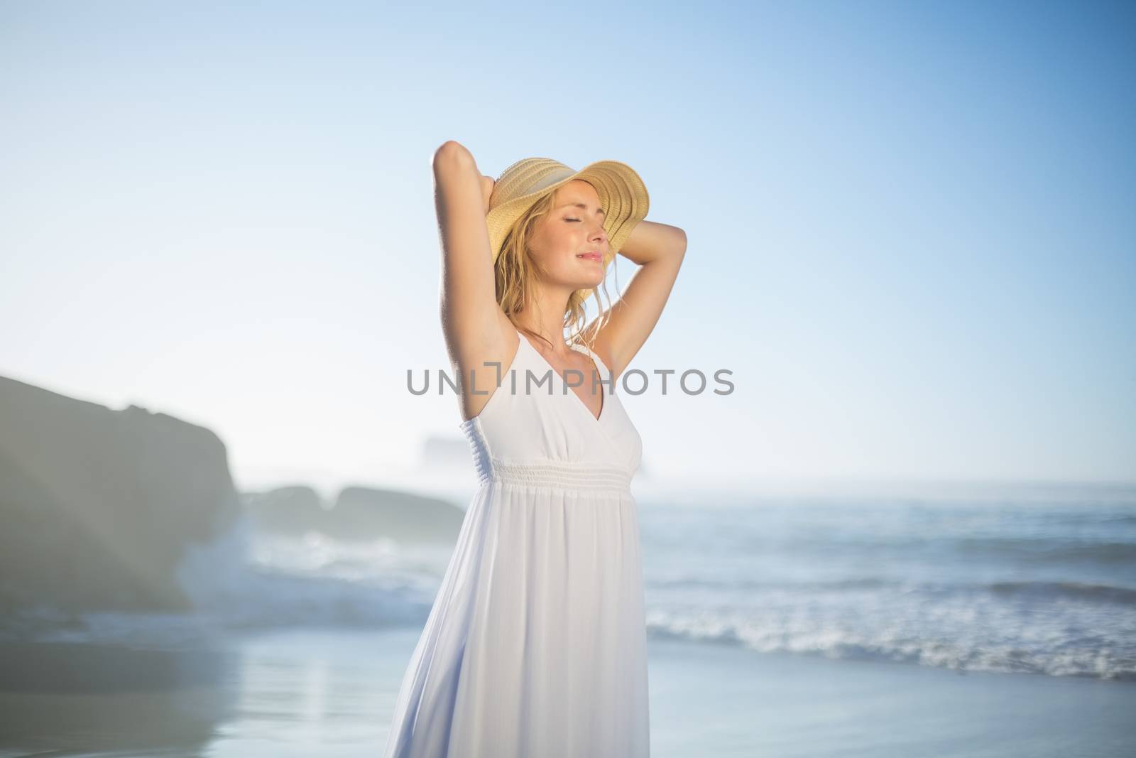 Smiling blonde standing at the beach in white sundress and sunhat by Wavebreakmedia