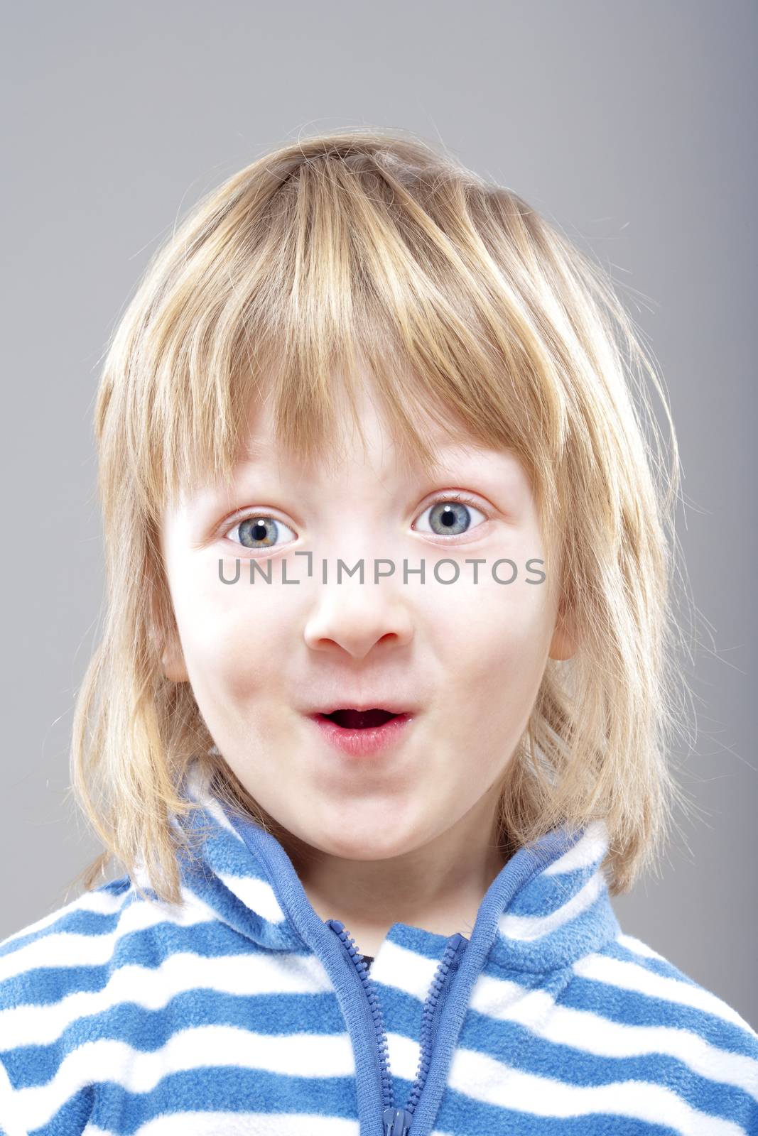 portrait of a boy with long blond hair smiling - isolated on gray