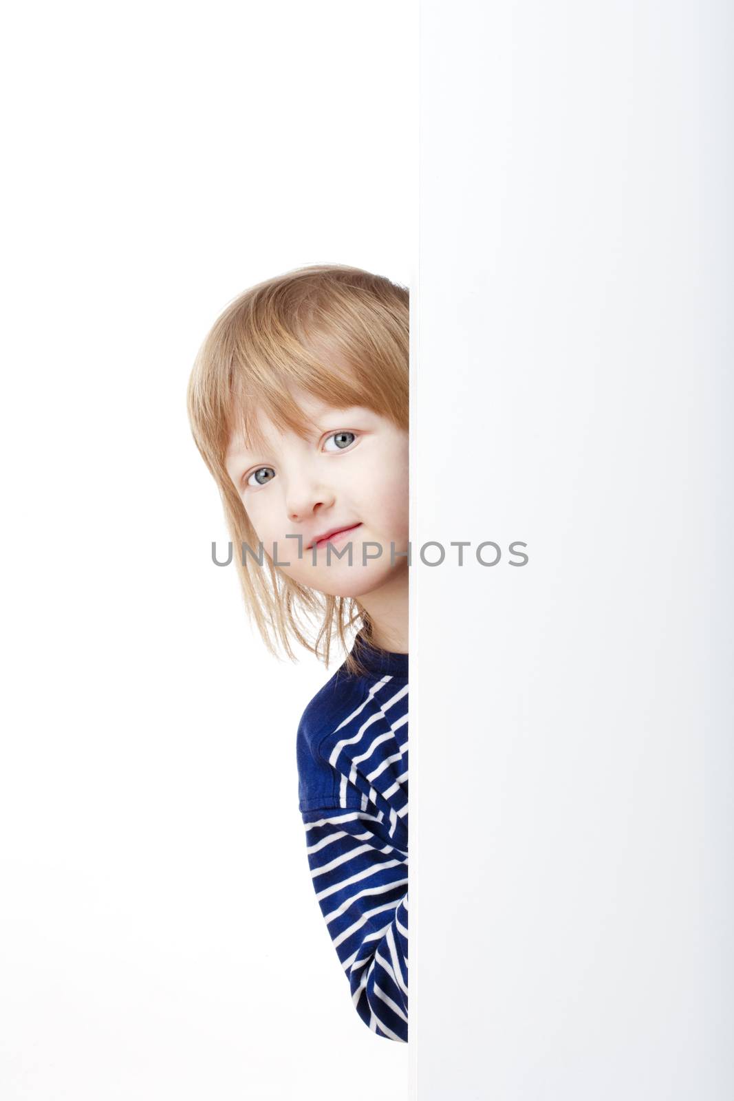 curious boy with long blond hair peeking out from behind a white board looking